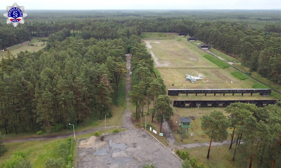 Zdjęcie z drona widok na byłą strzelnicę garnizonową, widoczny okoliczny las, oś strzelecka na środku której stoi samolot.