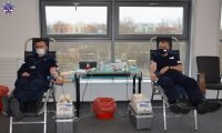 Dwóch policjantów siedzących na stanowiskach do pobierania krwi z podłączoną aparaturą.