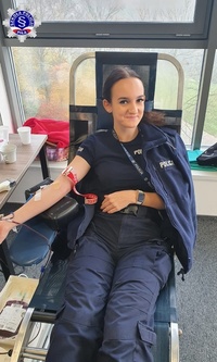 Kobieta w policyjnym mundurze, siedząc na fotelu oddaje krew i uśmiecha się do obiektywu.